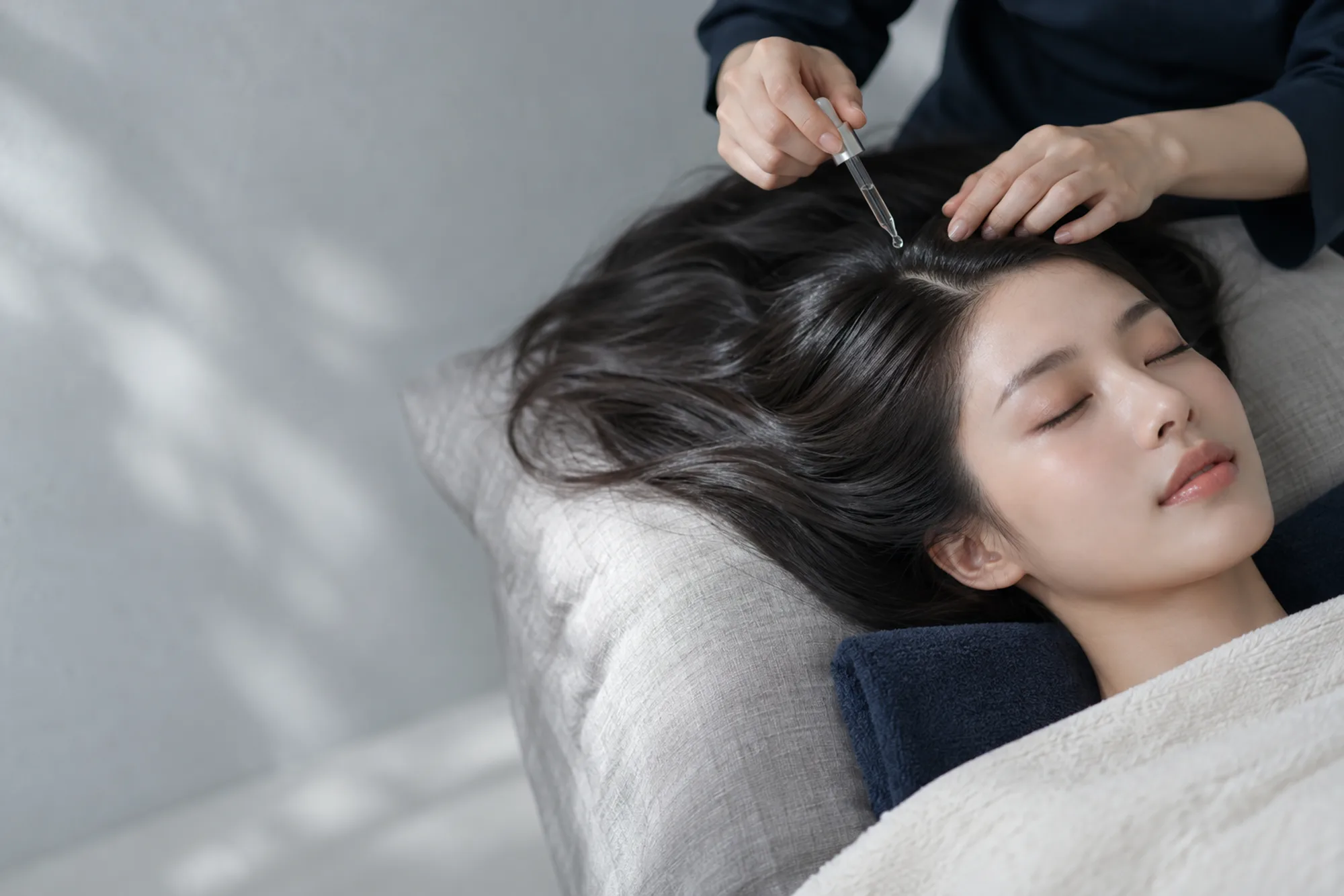 A therapist placing a drop of serum along a guest's hair parting